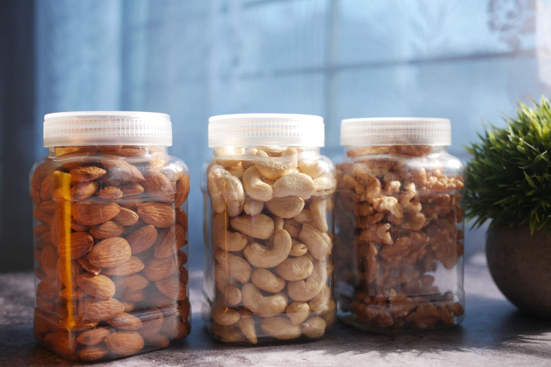 Plain plastic jars of cashews, almonds and walnuts on a table