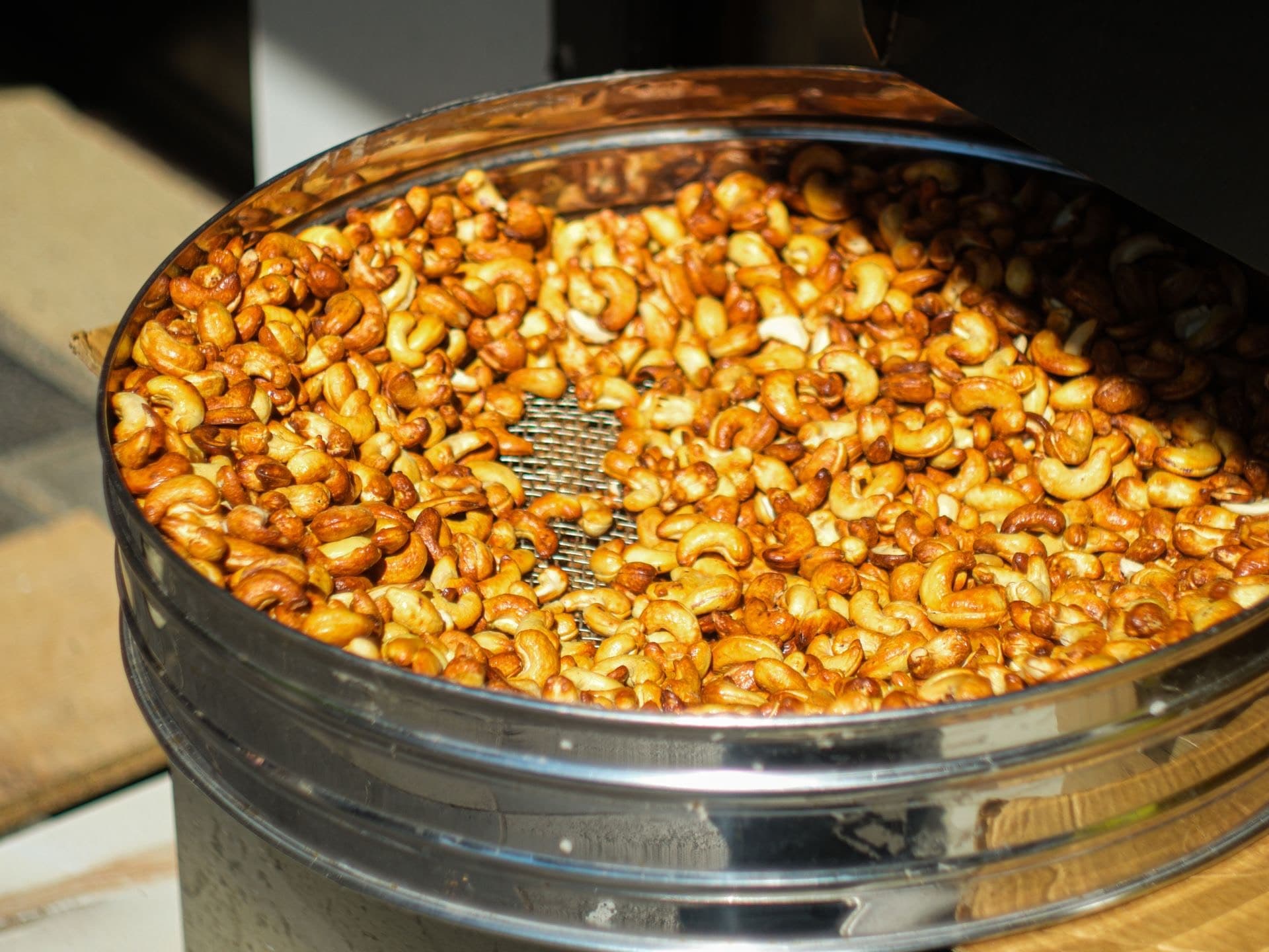 Freshly roasted cashews cooling in a round metal sieve