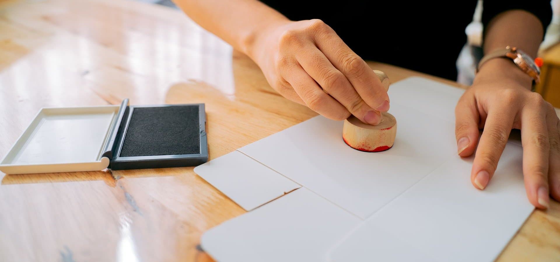 A hand pressing a wooden stamp onto white paper on a desk