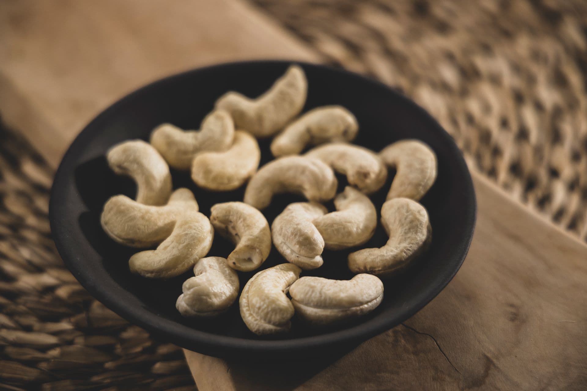 Whole cashew kernels counted out in a dark bowl