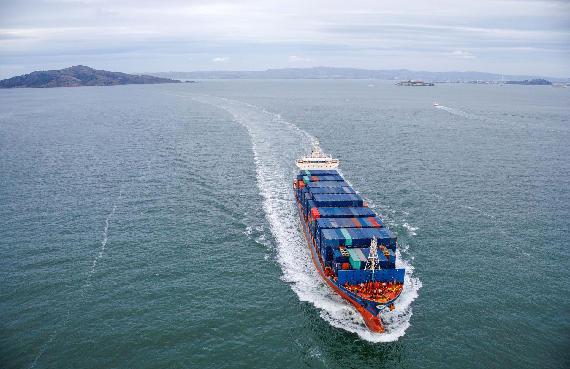 A loaded container ship at sea seen from above, leaving a white wake