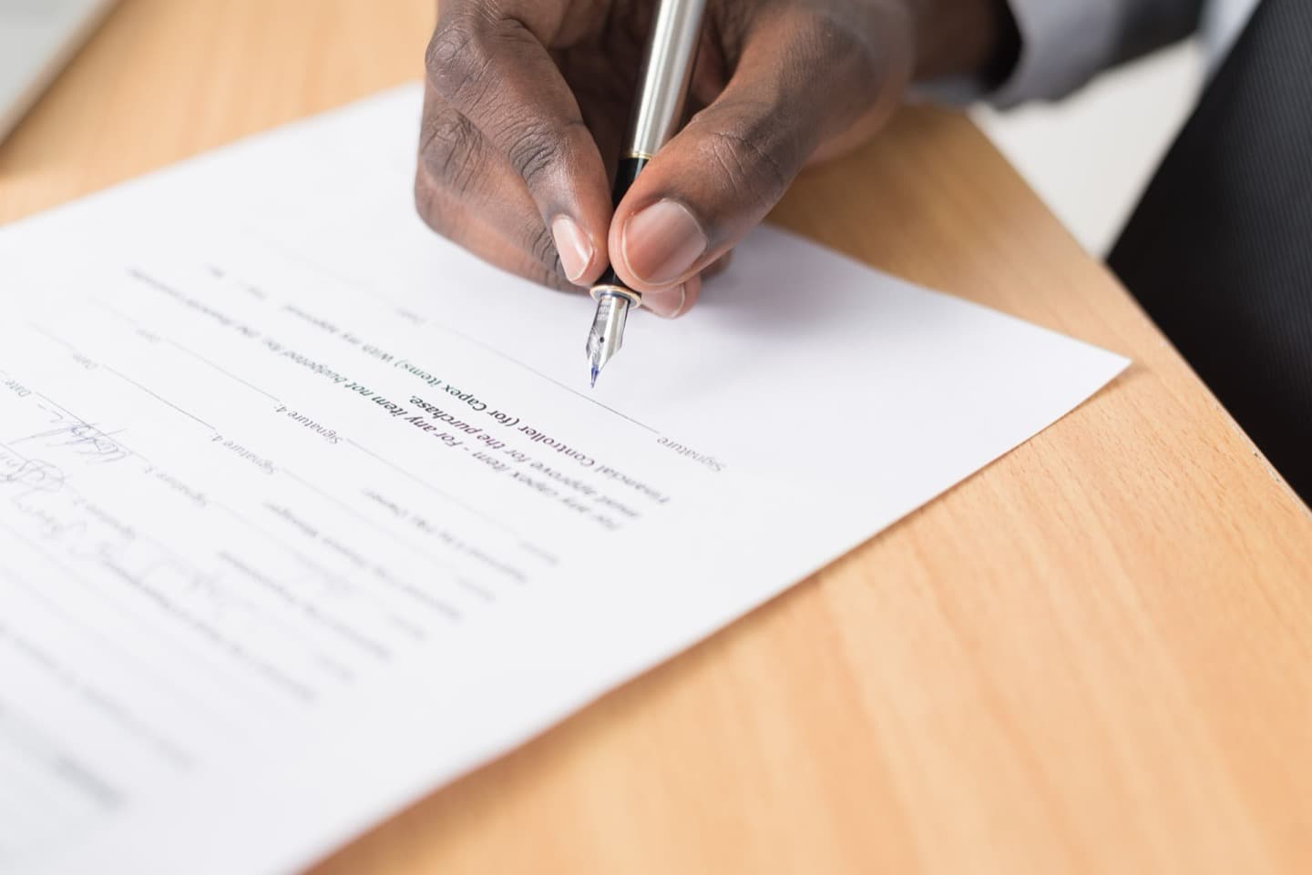 A hand signing a printed contract with a silver fountain pen